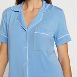 Woman wearing a light blue pajama top with white trim on a plain background