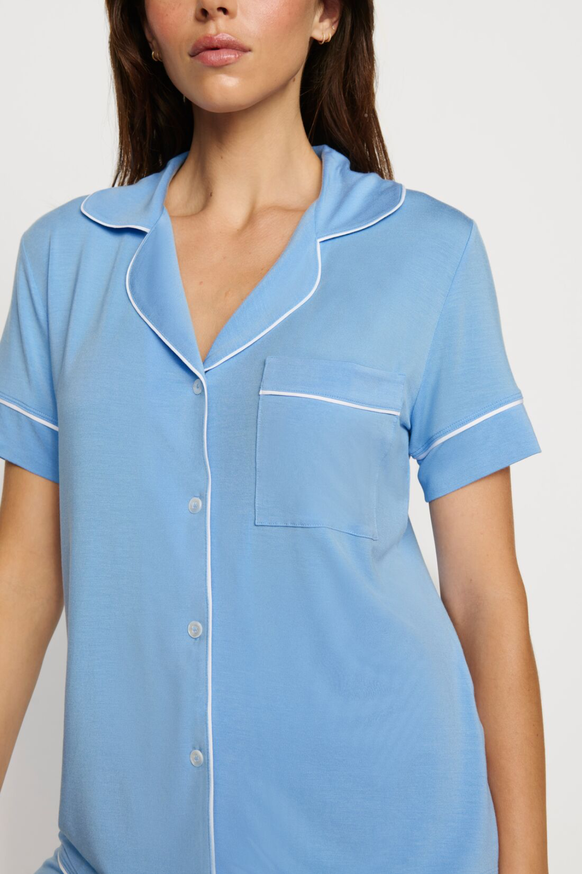 Woman wearing a light blue pajama top with white trim on a plain background