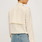 Woman wearing a cream jacket and blue jeans on a plain background