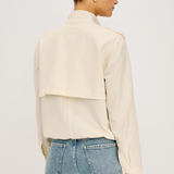 Woman wearing a cream jacket and blue jeans on a plain background