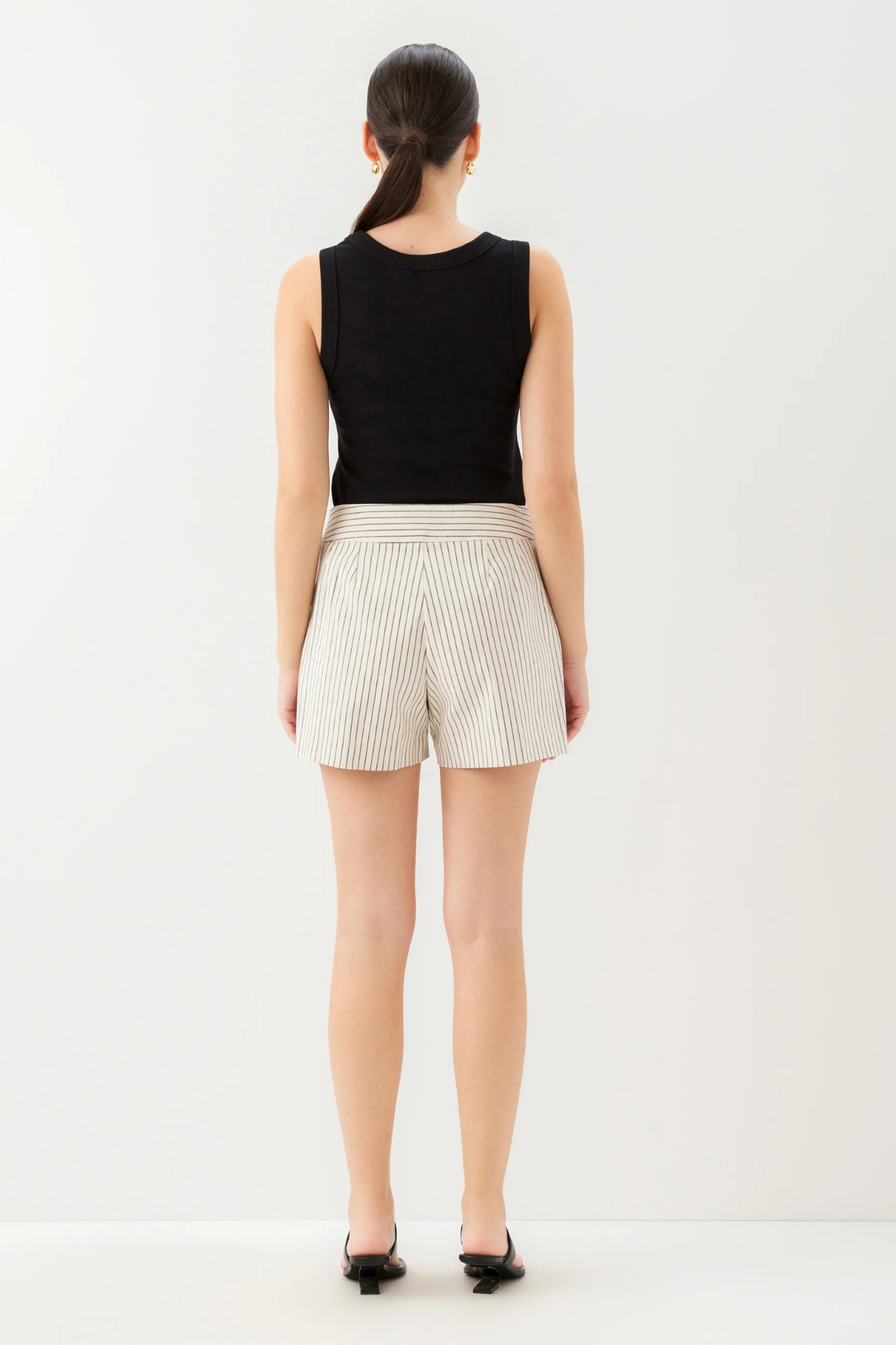 Person wearing a black sleeveless top and white striped shorts on a white background