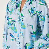 Light blue blouse with colorful floral pattern worn by a person on a white background