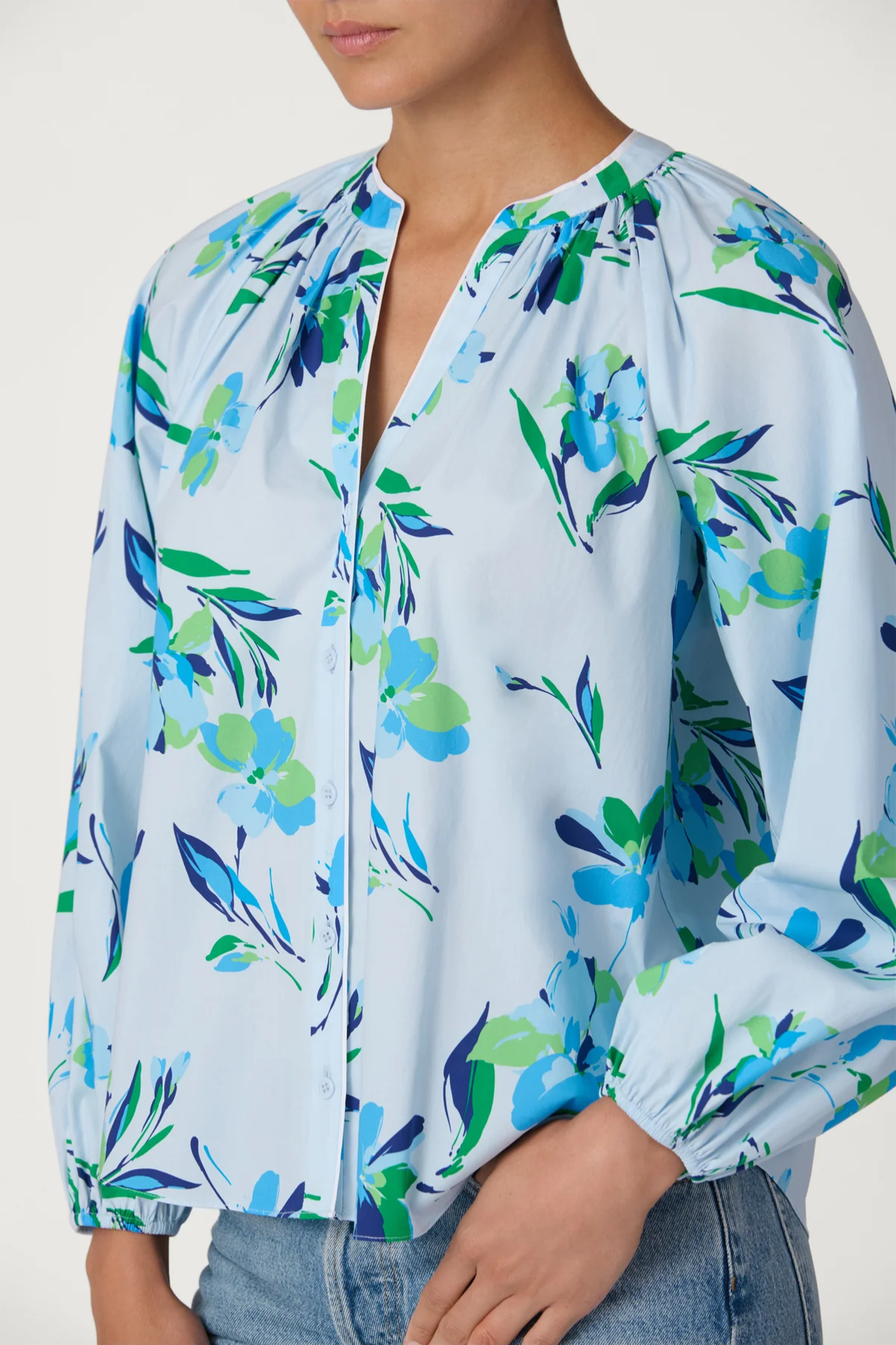 Light blue blouse with colorful floral pattern worn by a person on a white background