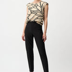 Woman wearing a patterned top and black pants on a white background