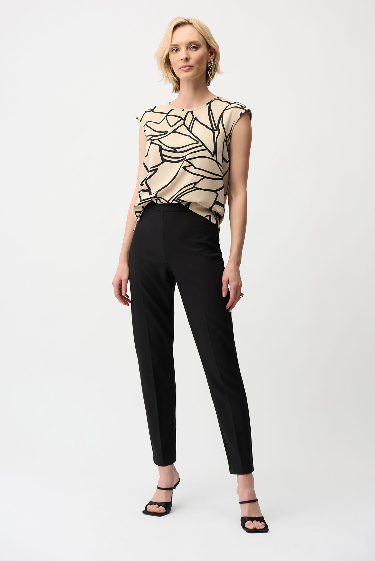 Woman wearing a patterned top and black pants on a white background