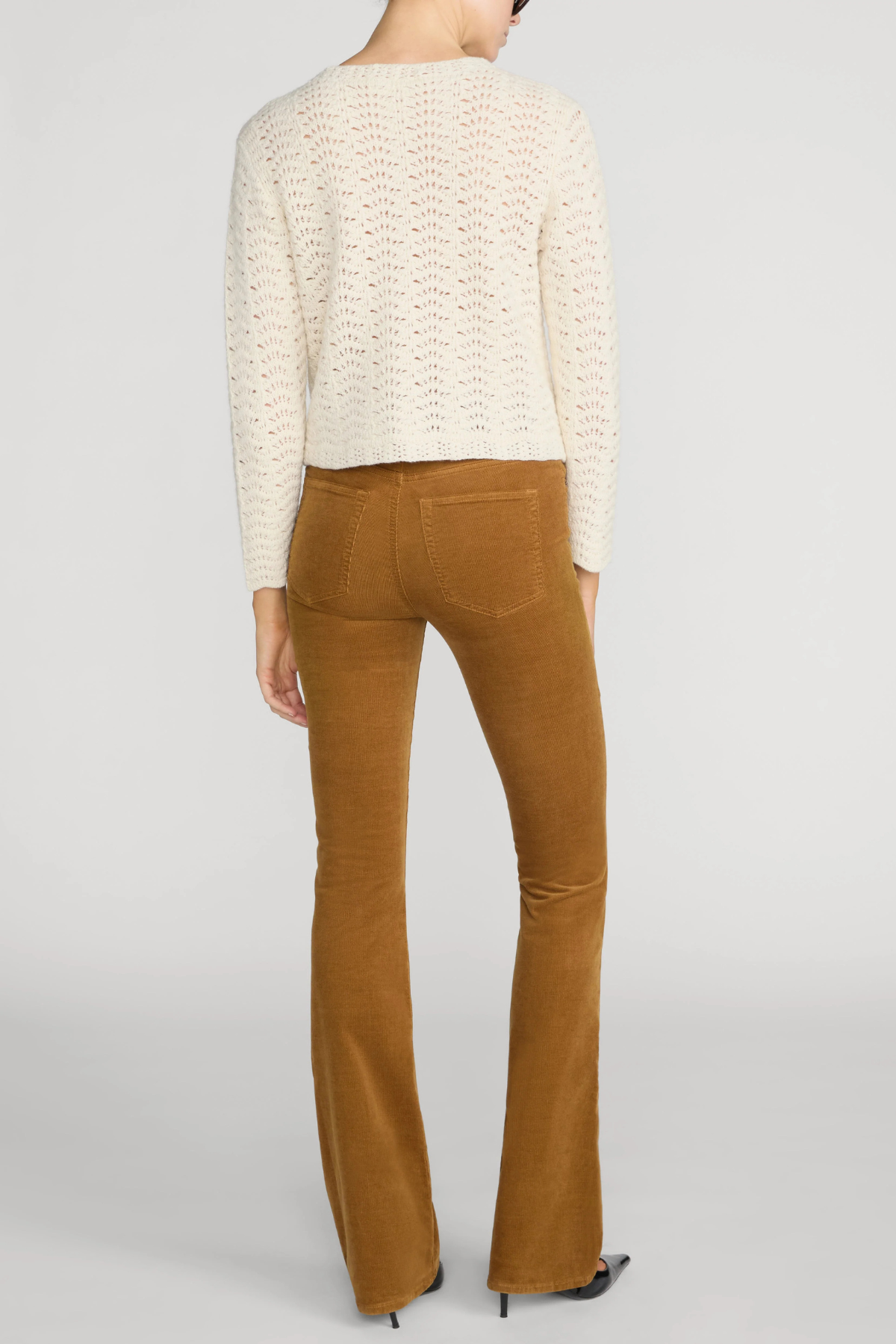 Rear view of a model wearing a cream cable-knit cropped sweater and brown corduroy flare pants against a light gray studio background.