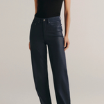 A model wearing a black sleeveless top and dark navy wide-leg jeans, standing against a light gray studio background.