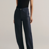 A model wearing a black sleeveless top and dark navy wide-leg jeans, standing against a light gray studio background.