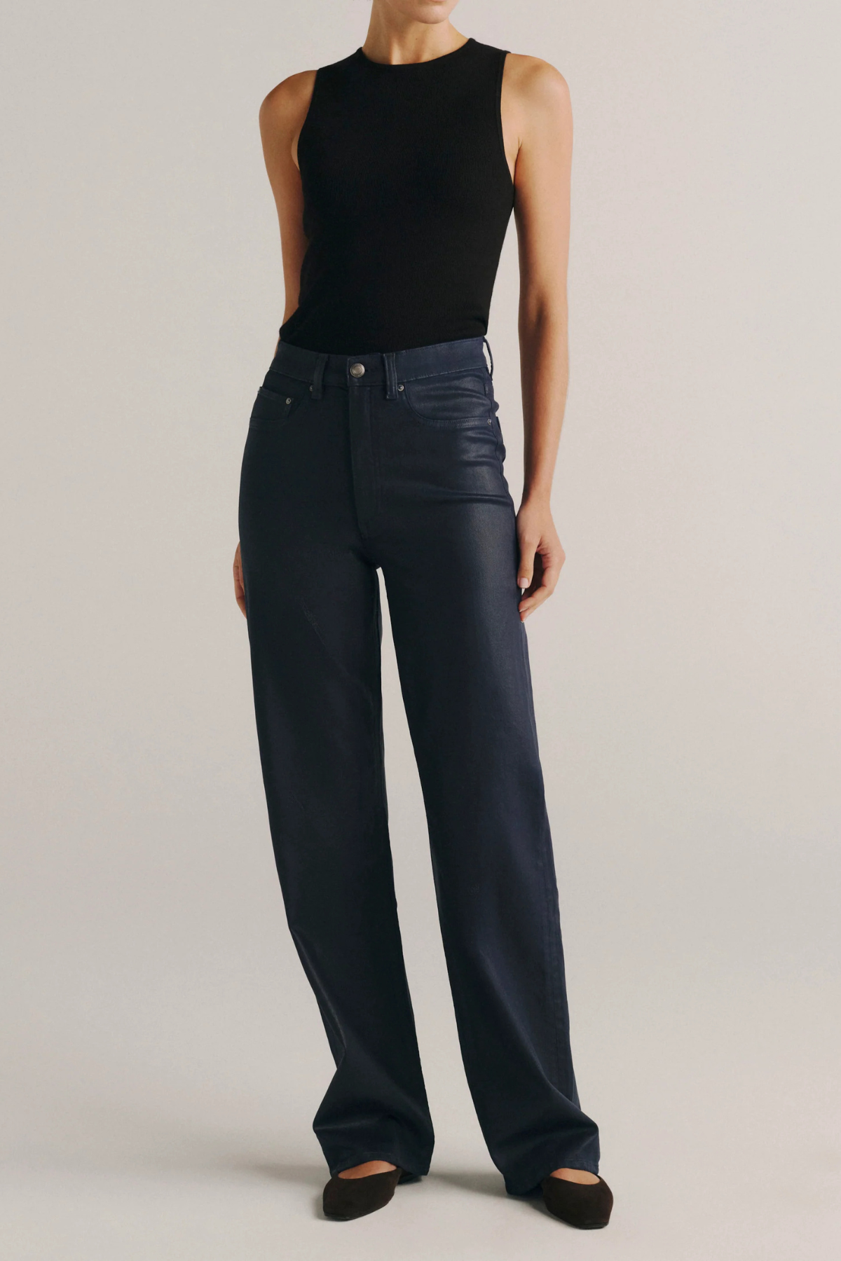 A model wearing a black sleeveless top and dark navy wide-leg jeans, standing against a light gray studio background.
