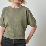 Woman wearing a green t-shirt and dark jeans against a plain background