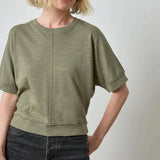 Woman wearing a green t-shirt and dark jeans against a plain background