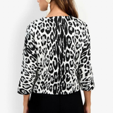 A woman shown from the back wearing a black and white leopard print top with three-quarter sleeves and black pants, against a plain white background.
