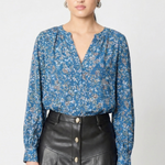 model wearing a long sleeve printed blue blouse with a v neck line and a black leather skirt with buttons against a white background