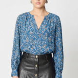 model wearing a long sleeve printed blue blouse with a v neck line and a black leather skirt with buttons against a white background