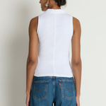 Person wearing a white sleeveless top and blue jeans against a plain background