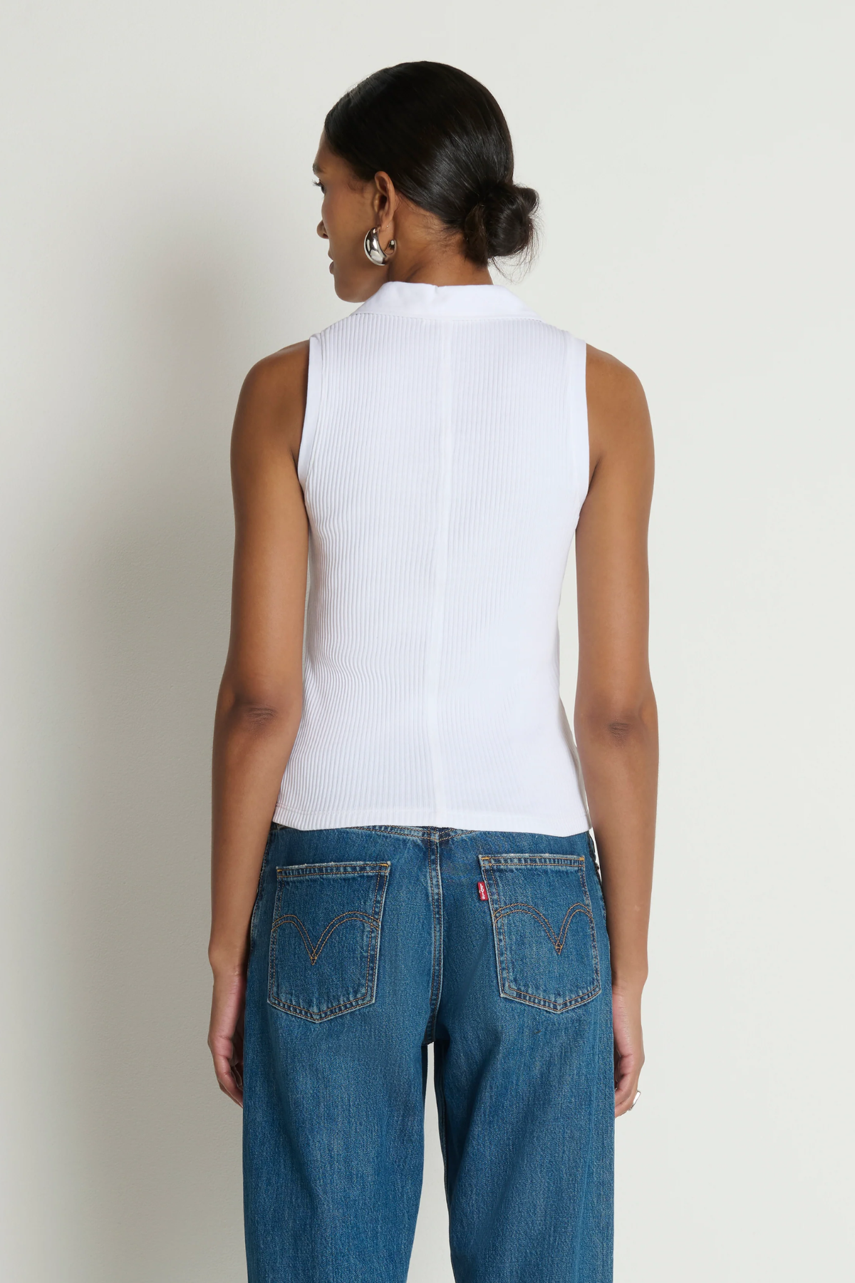 Person wearing a white sleeveless top and blue jeans against a plain background
