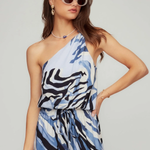 Woman wearing a blue and black patterned dress with sunglasses on a plain background
