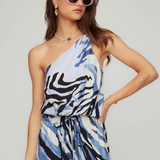 Woman wearing a blue and black patterned dress with sunglasses on a plain background