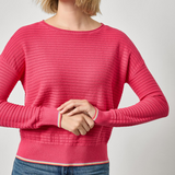 Woman wearing a pink sweater and blue jeans on a light gray background