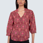 A woman modeling a patterned blouse with a split V-neck and three-quarter sleeves, paired with black pants, against a light gray studio background.
