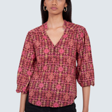 A woman modeling a patterned blouse with a split V-neck and three-quarter sleeves, paired with black pants, against a light gray studio background.