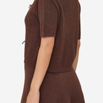 A woman shown from the back wearing a brown short-sleeve knit sweater and matching brown skirt against a plain light background.