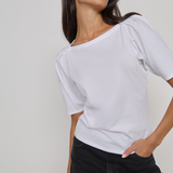 Woman wearing a white top and black pants against a plain background