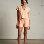 Woman wearing a peach-colored outfit standing against a plain wall.