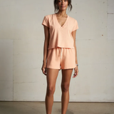 Woman wearing a peach-colored outfit standing against a plain wall.