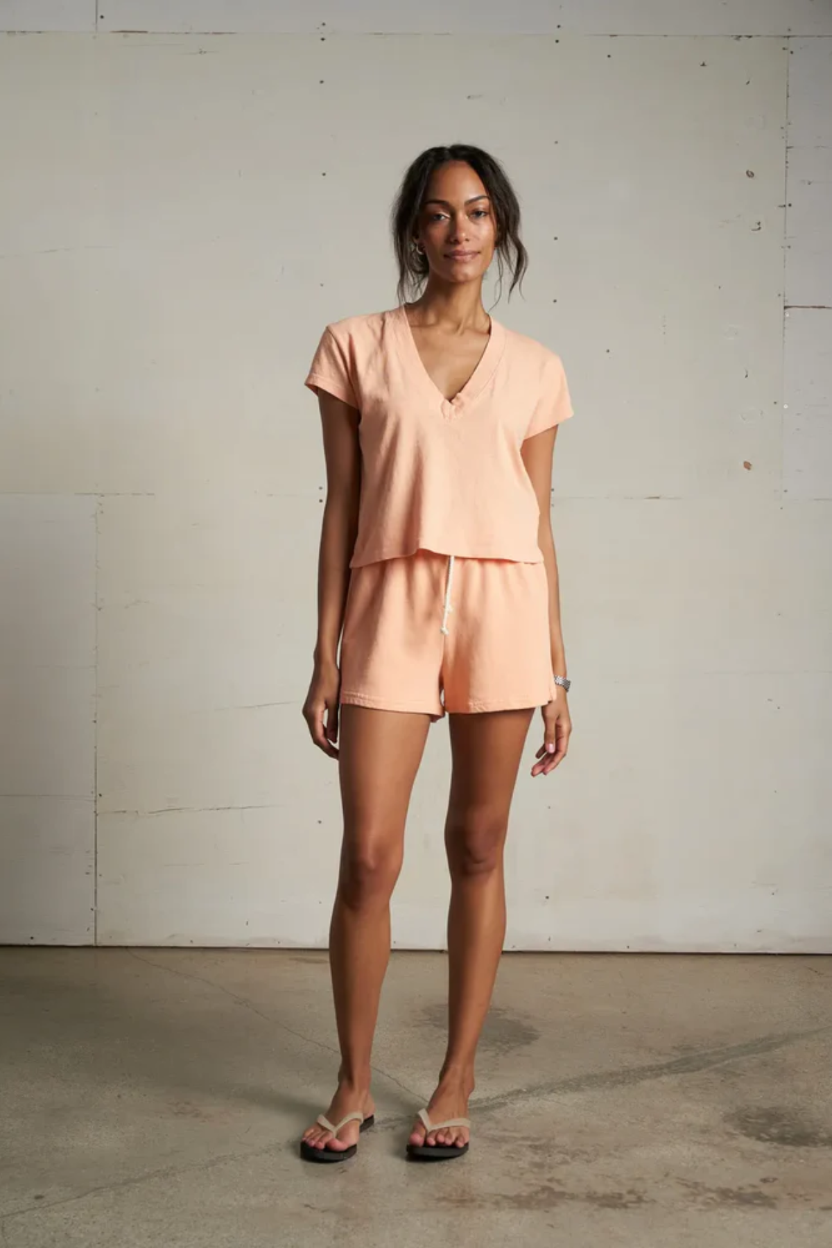 Woman wearing a peach-colored outfit standing against a plain wall.