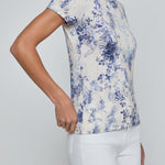 Woman wearing a blue floral print top and white pants on a plain background
