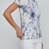 Woman wearing a blue floral print top and white pants on a plain background
