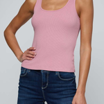 A woman wearing a fitted scoop-neck tank top in dusty pink with dark blue jeans, shown from the nose down against a light gray studio background.
