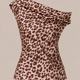 A one-shoulder leopard print top with a draped, cowl-like neckline and a fitted silhouette, shown against a solid beige background.