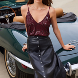 A woman posing in front of a classic green convertible car, wearing a burgundy sequined spaghetti-strap top and a black faux-leather midi skirt with a silver button-down front.