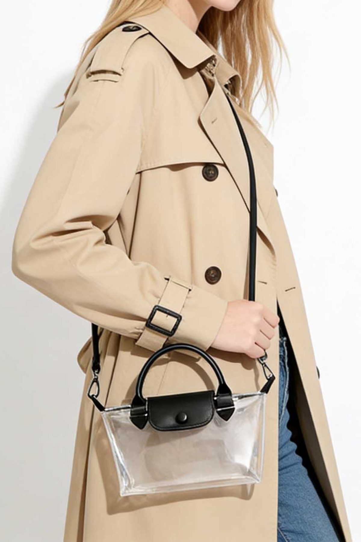 Person wearing a beige trench coat holding a clear handbag with a black handle.