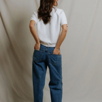 back of woman in white top and denim on draped background 