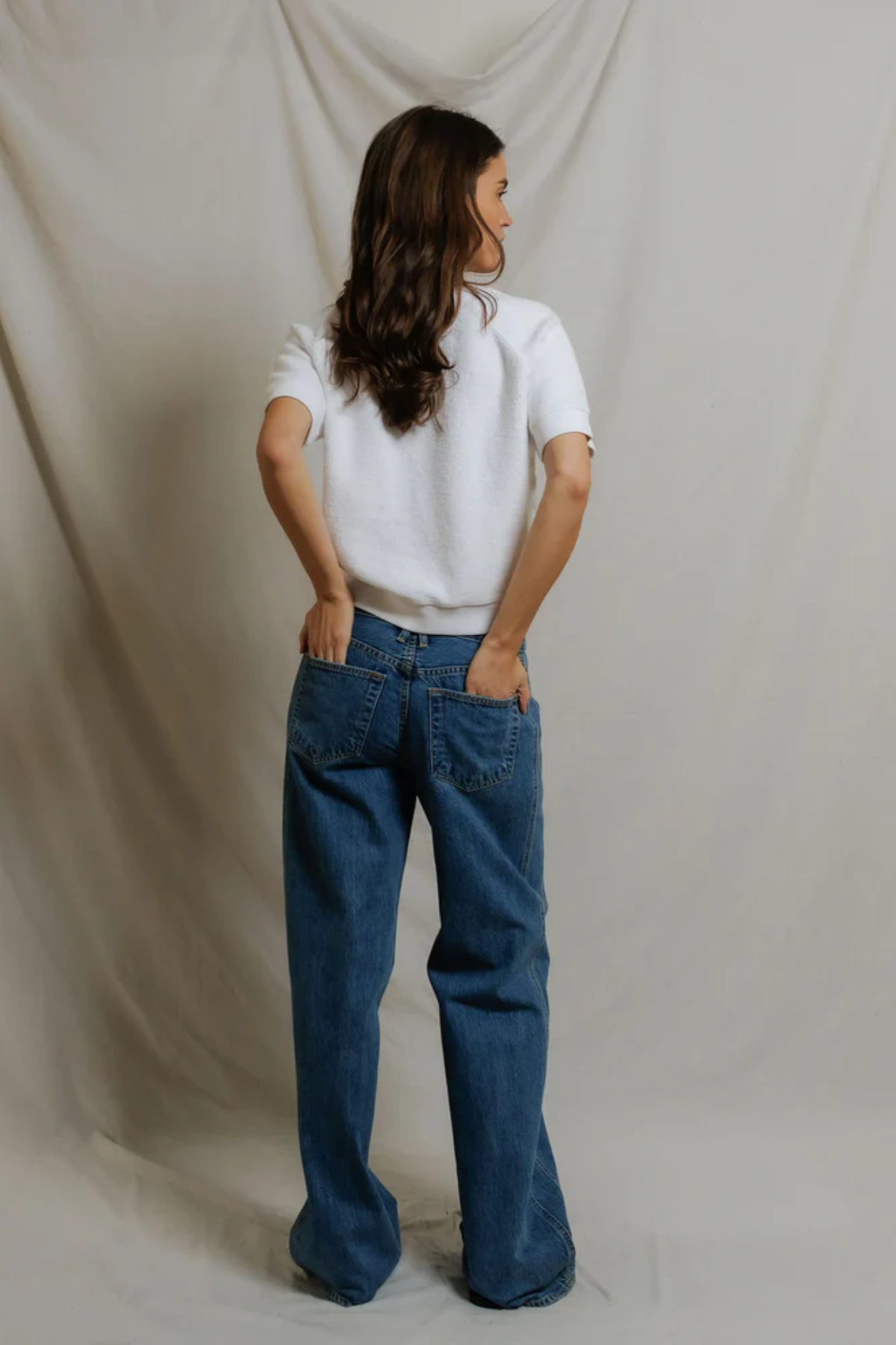 back of woman in white top and denim on draped background 