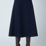 A dark navy blue A-line midi skirt shown on a model from the waist down, paired with brown leather knee-high boots against a light gray studio background.