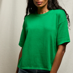 Woman wearing a green t-shirt and blue jeans against a neutral background