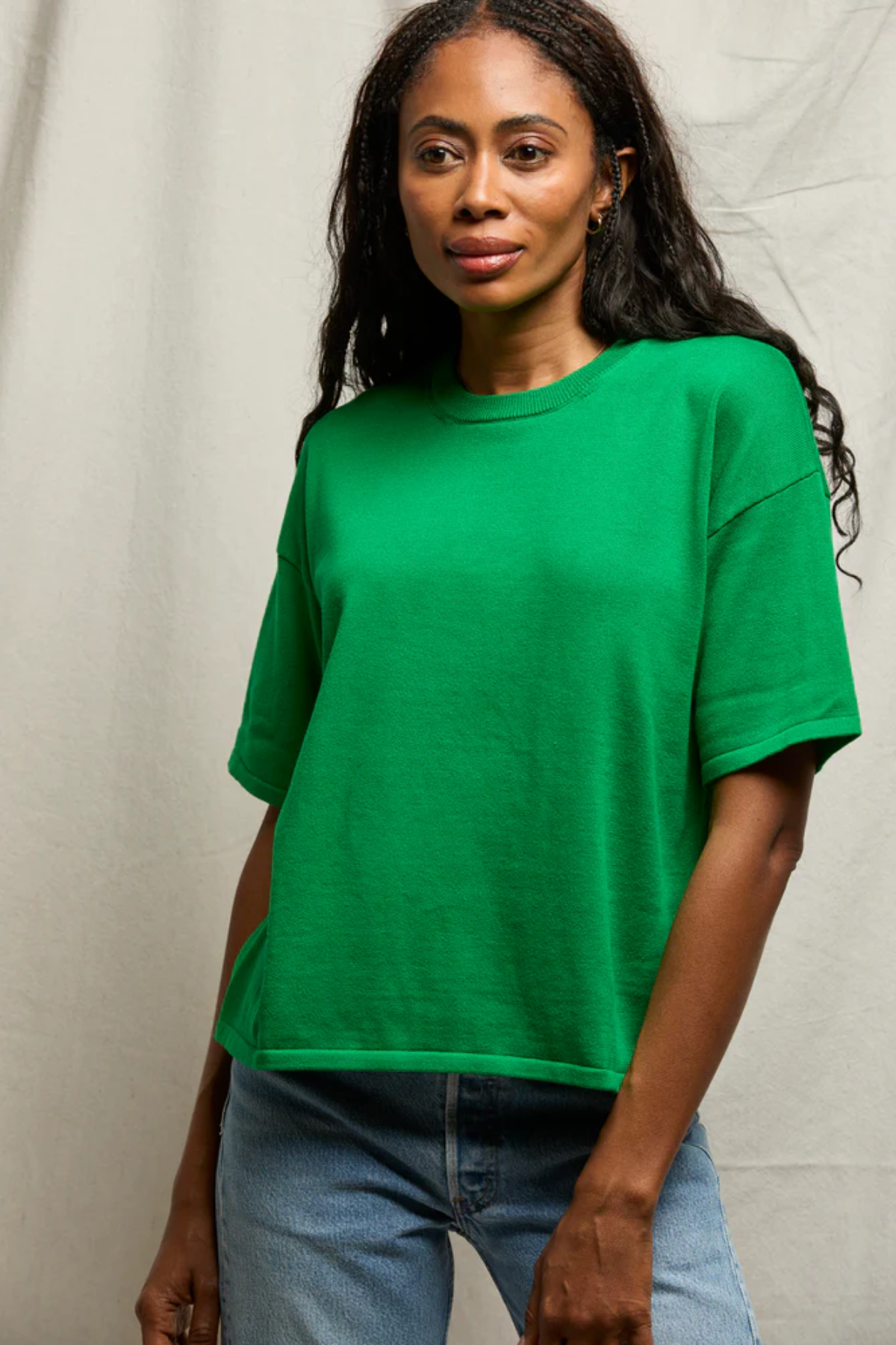 Woman wearing a green t-shirt and blue jeans against a neutral background