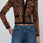 A woman wearing a cropped leopard-print cardigan with a black collar and front buttons, paired with blue jeans, against a light gray studio background.