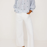Person wearing a blue patterned blouse, white pants, and black flats on a white background