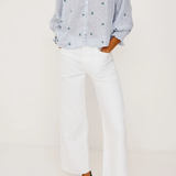 Person wearing a blue patterned blouse, white pants, and black flats on a white background