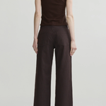 A model shown from the back wearing a sleeveless dark brown mock-neck top and dark brown pinstriped wide-leg trousers, set against a plain light gray studio background.