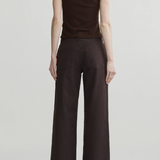 A model shown from the back wearing a sleeveless dark brown mock-neck top and dark brown pinstriped wide-leg trousers, set against a plain light gray studio background.