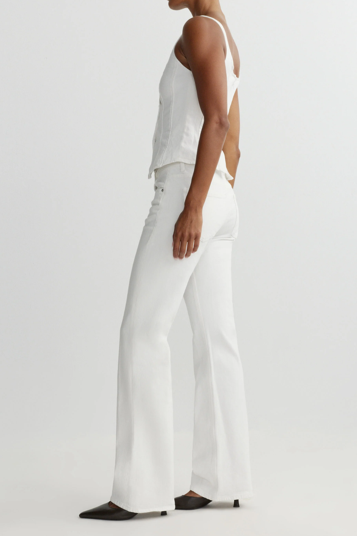 Person wearing a white sleeveless top and white denim on a light gray background