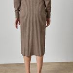 A model from the back wearing a taupe ribbed knit midi skirt and matching knit sweater, paired with tan heeled sandals, set against a neutral studio backdrop.