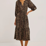 A woman modeling a leopard-print midi dress with three-quarter sleeves and a V-neckline, paired with black flats, against a plain white studio background.