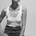 Person wearing a white tank top and high-waisted jeans against a plain background